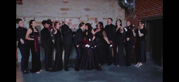 A wedding party in black formalwear against a brick wall